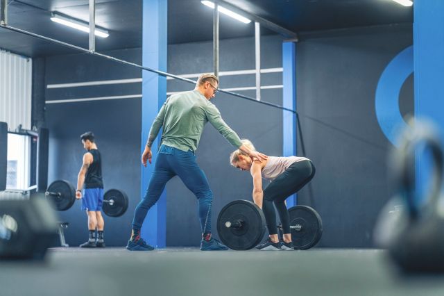 Femme et entraîneur soulevant des poids dans un gymnase.